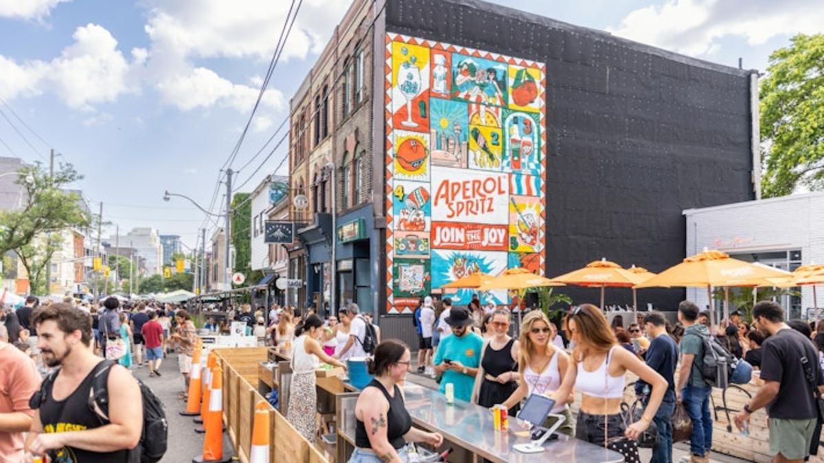 People gathered at a crowded street bar with orange umbrellas